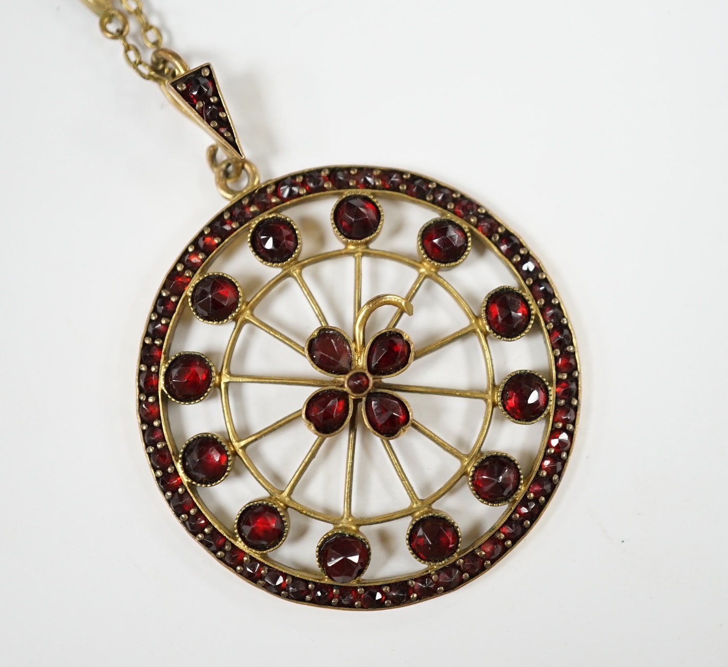 A late Victorian gilt metal and garnet cluster set 'wheel' pendant on a garnet set chain, overall 48cm. Condition - poor to fair